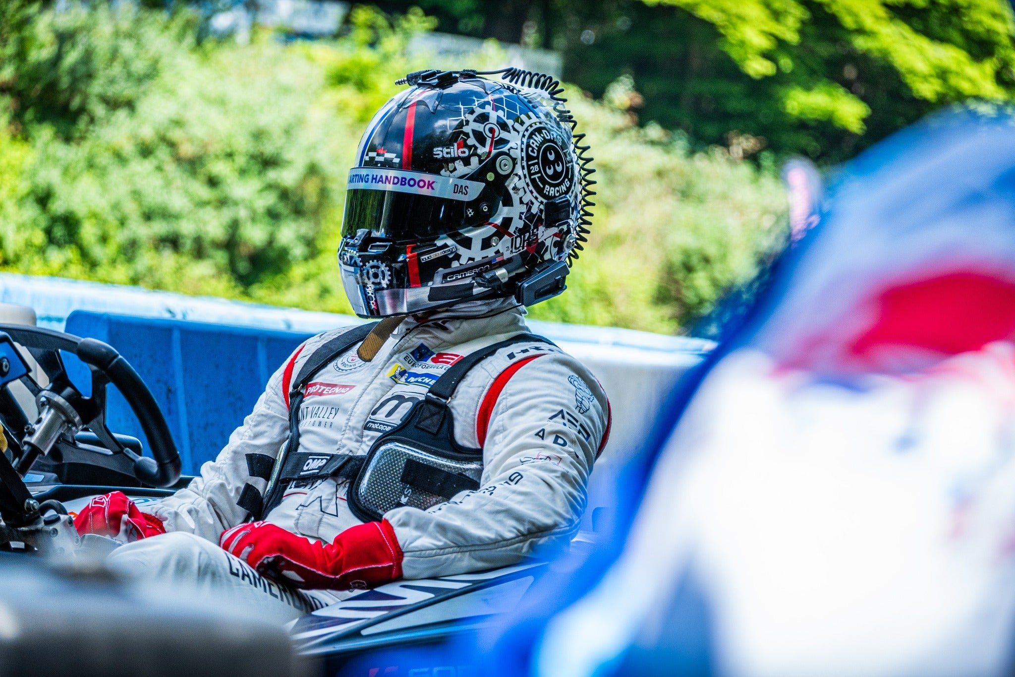 Cam Das in a racing suit and helmet with visor sticker sitting in a go-kart with blurred background